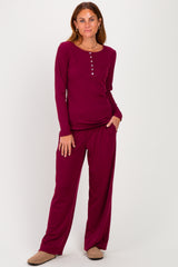 woman wearing a burgundy long sleeve loungewear set with buttons and matching pants, standing hands in pockets