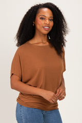 woman wearing a rust-colored oversized short sleeve top and blue jeans, smiling at the camera