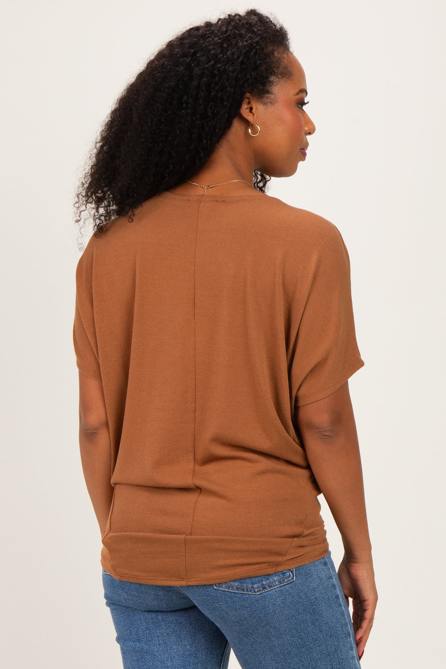 woman wearing a brown short sleeve top with a relaxed fit, styled with blue jeans, seen from the back