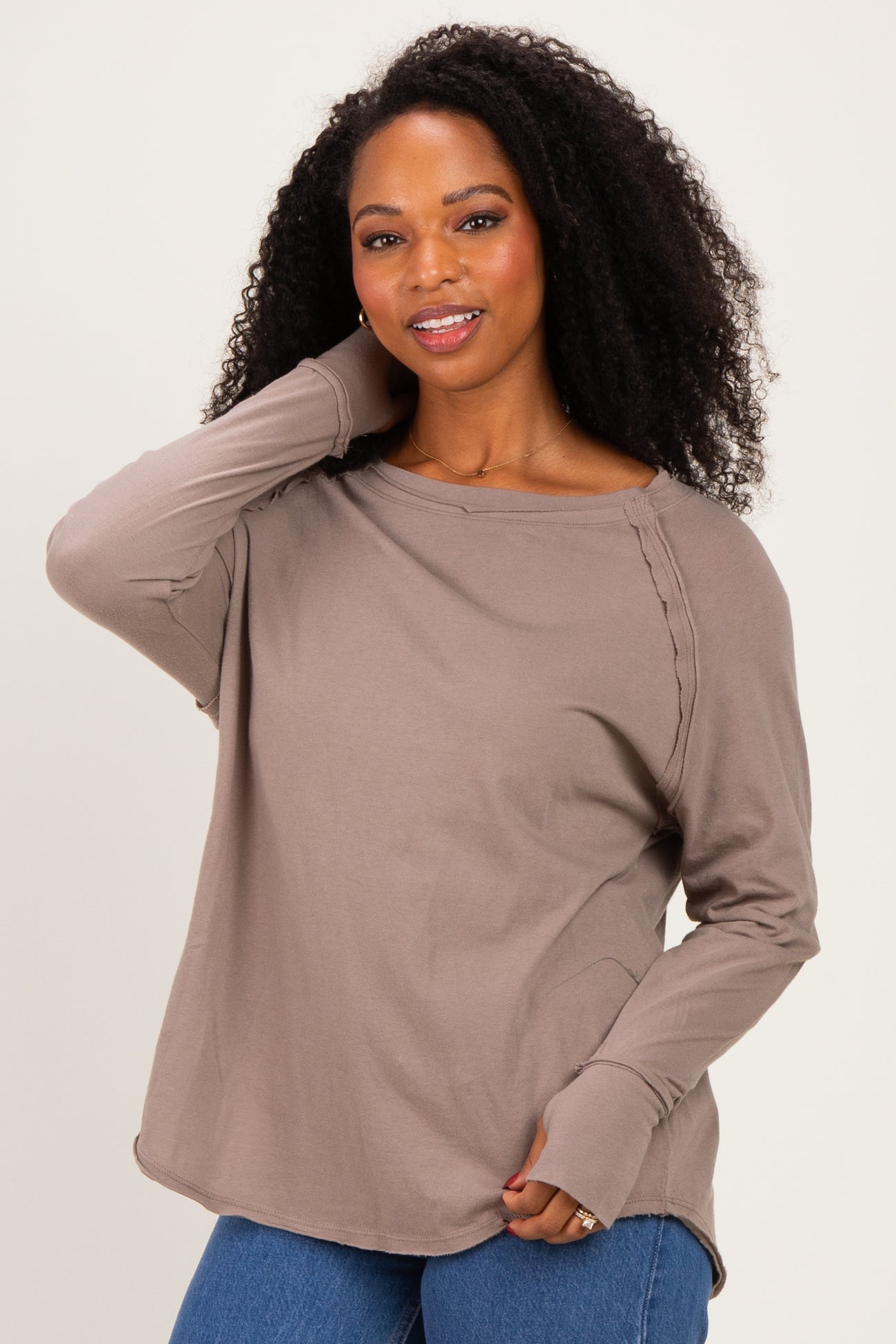 woman wearing a taupe long sleeve top with side detailing and relaxed fit, posing with one hand on her head