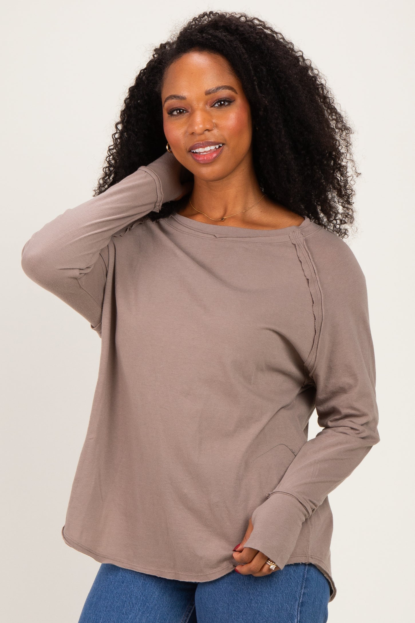 woman wearing a taupe long sleeve top with side detailing and relaxed fit, posing with one hand on her head