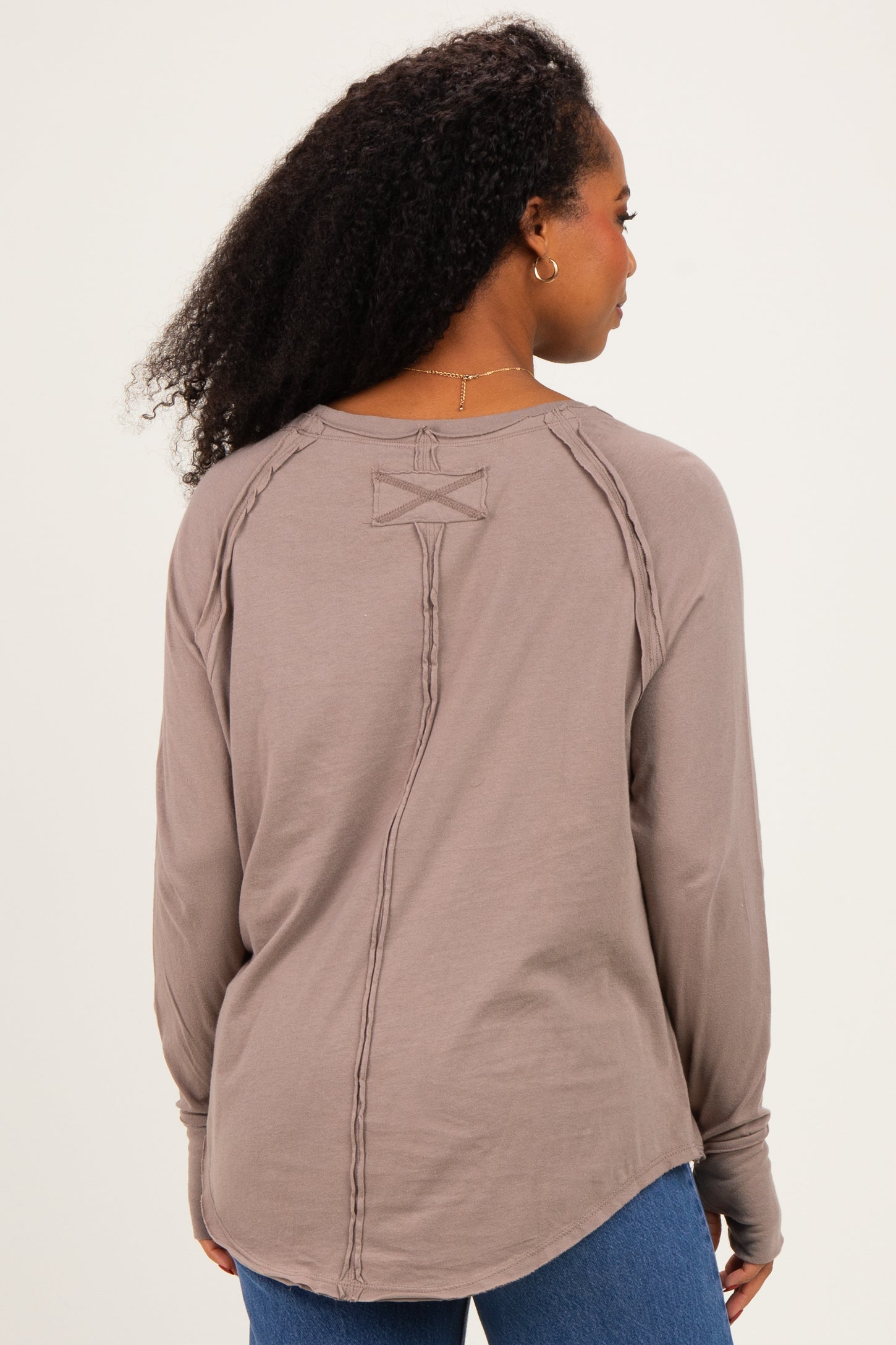 woman wearing a light brown long sleeve top with a unique back detail and relaxed fit