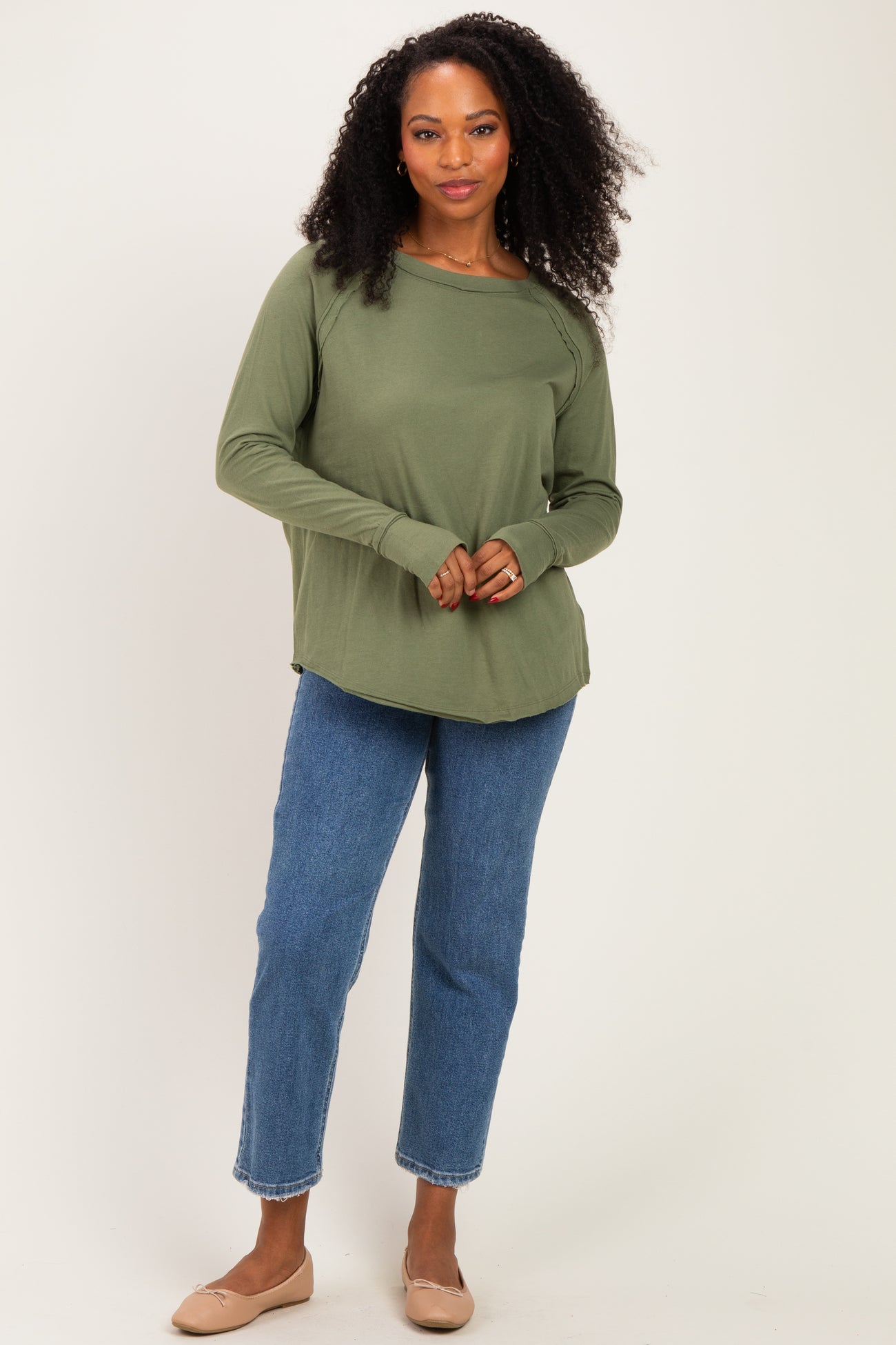 woman wearing a green long sleeve top and blue straight leg jeans, posing with one hand on her hip