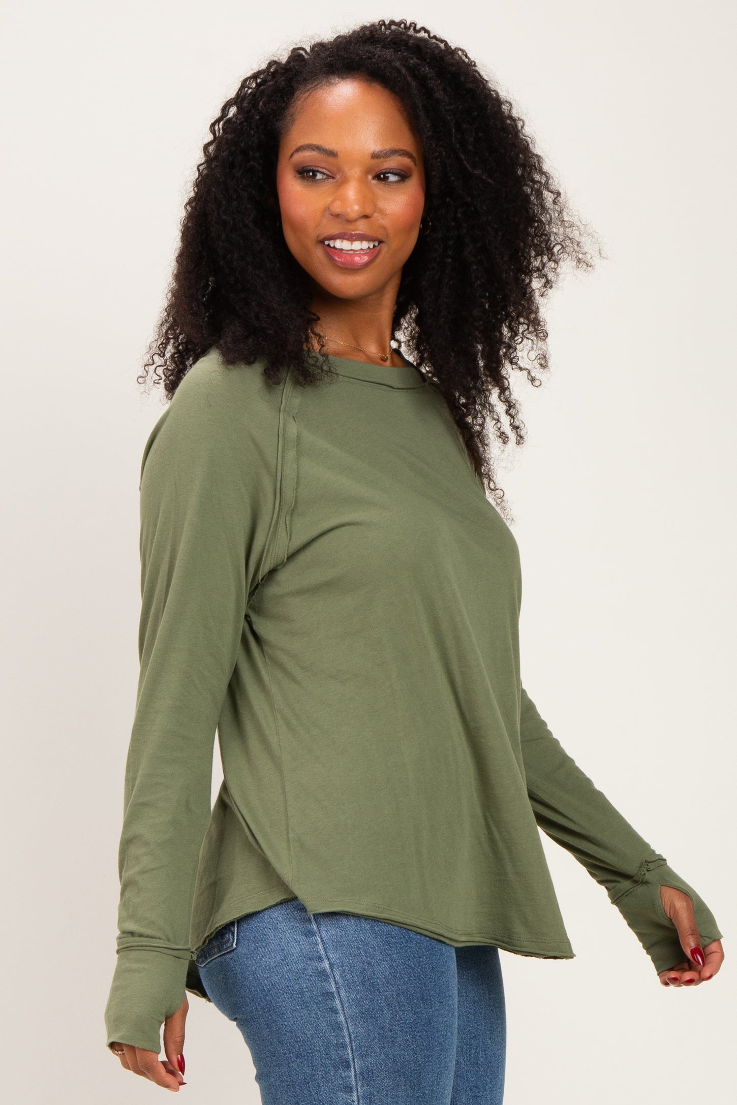 woman wearing an olive green long sleeve top with side slits and thumbholes, paired with blue jeans
