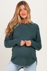 woman wearing a dark teal maternity sweater with long sleeves and a maternity-friendly fit, holding her baby bump