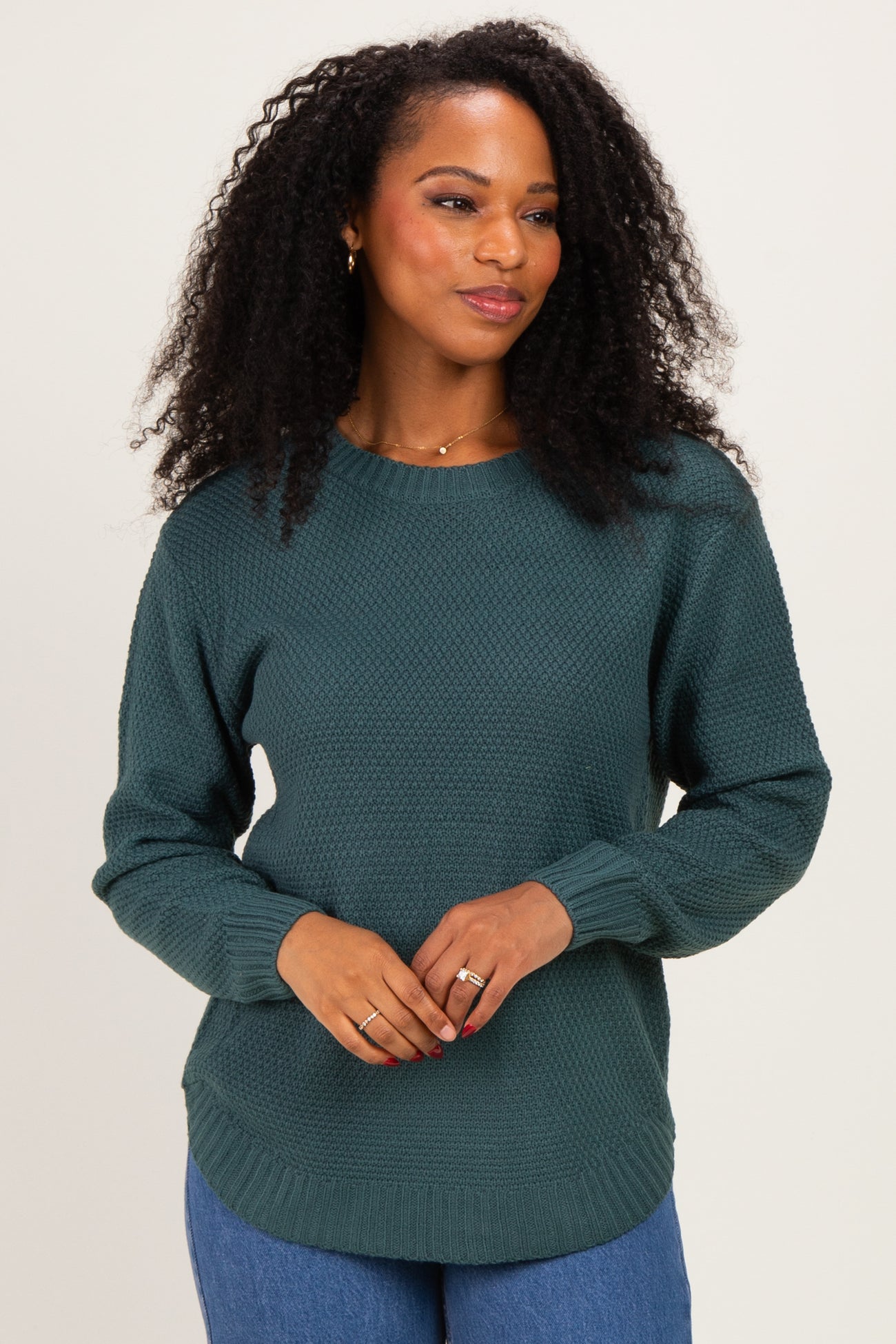 woman wearing a dark green textured long sleeve sweater and smiling, paired with blue jeans