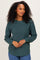 woman wearing a dark green textured long sleeve sweater and smiling, paired with blue jeans