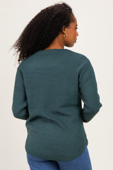 woman wearing a dark teal textured sweater, standing with her back to the camera, paired with blue jeans