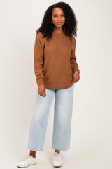 woman wearing a brown textured sweater and light blue wide-leg jeans, posing with one hand on her hip