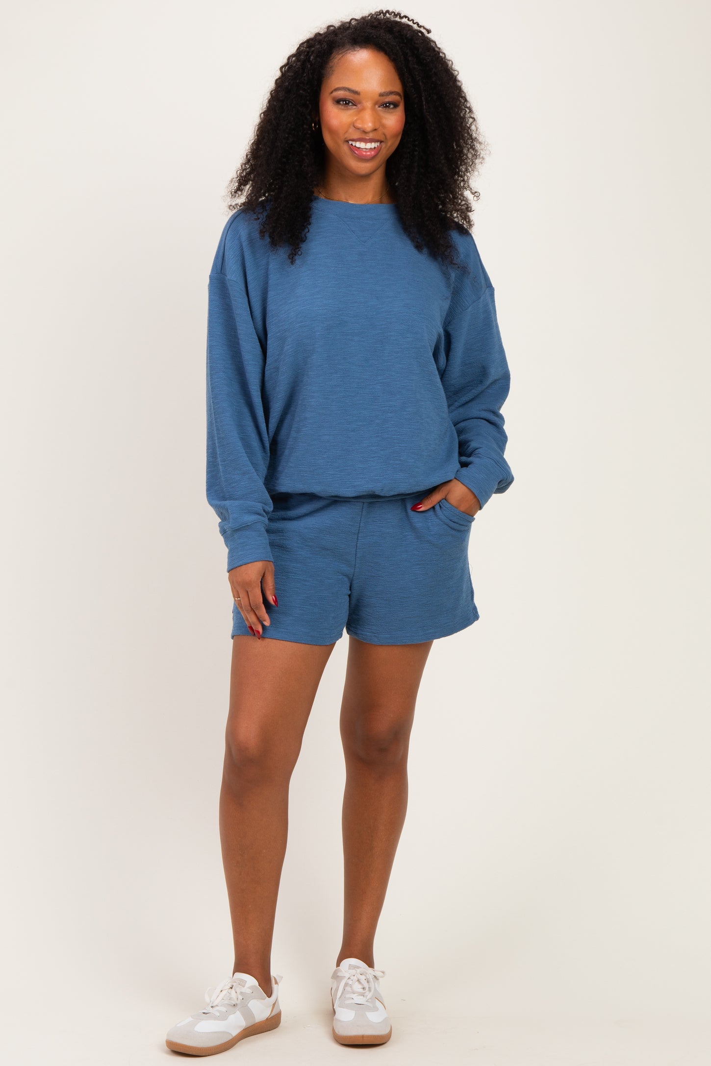 woman wearing a blue cozy sweatshirt and matching shorts, styled with white sneakers
