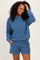 woman wearing a blue sweatshirt and matching shorts, smiling and touching her hair