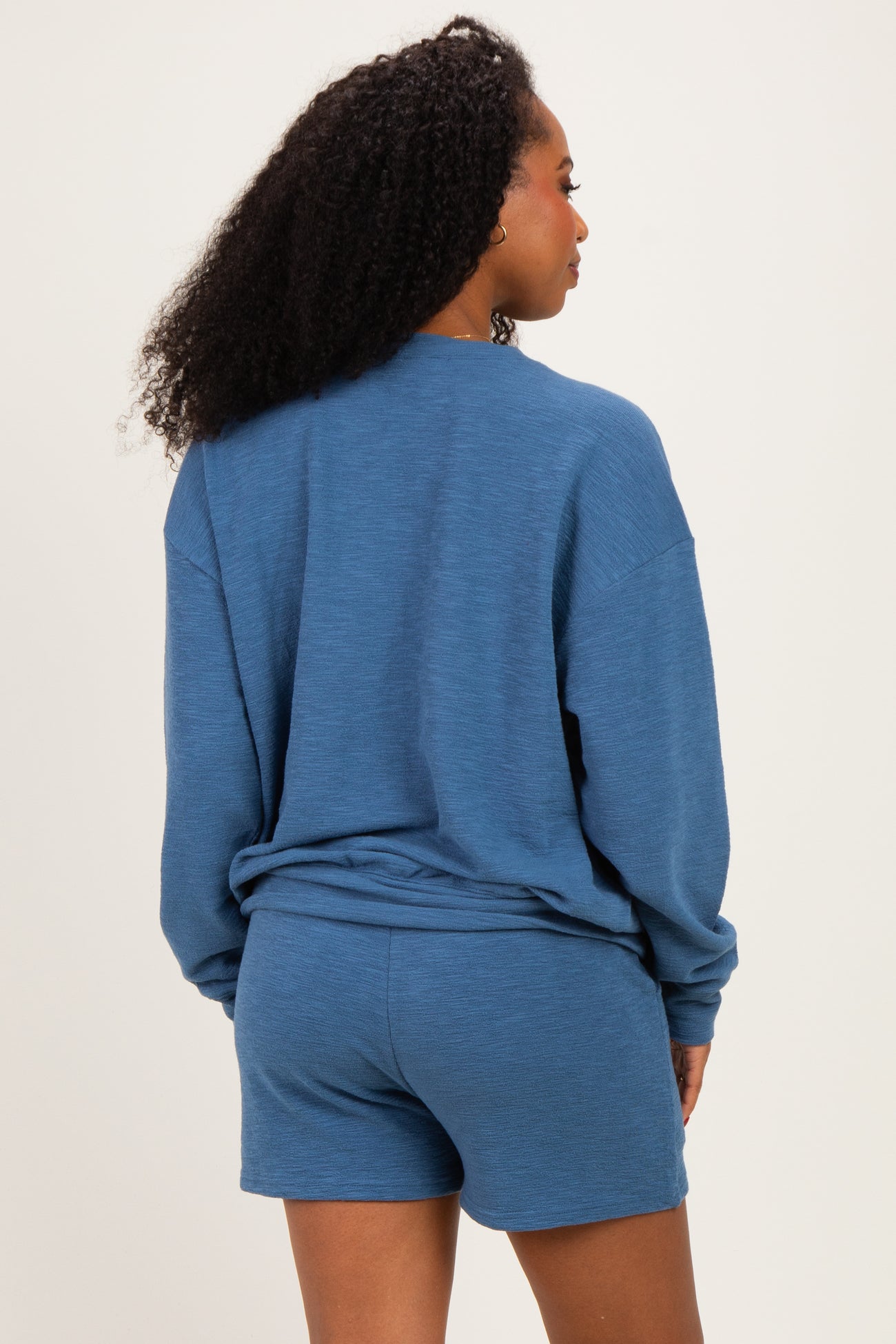 woman wearing a blue oversized sweatshirt and matching shorts, seen from the back, showcasing a casual loungewear look