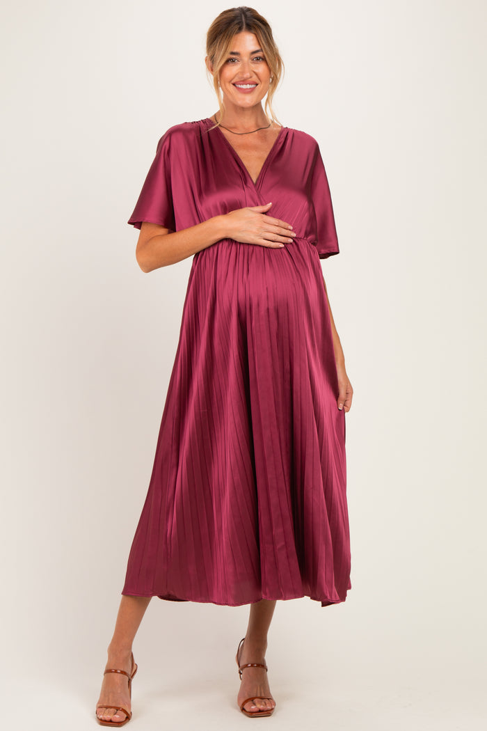 woman wearing a deep burgundy maternity dress with short sleeves and a pleated skirt, holding her baby bump