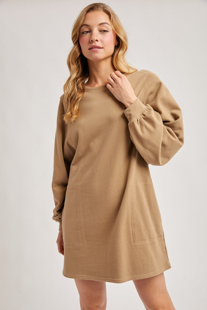 woman wearing a camel-colored long sleeve sweatshirt dress with side pockets and a relaxed fit