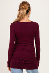 woman wearing a burgundy long sleeve maternity top with ruching detail at the waist
