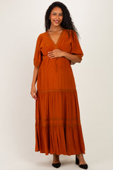woman wearing an orange maternity maxi dress with puff sleeves and a v-neck, holding her baby bump