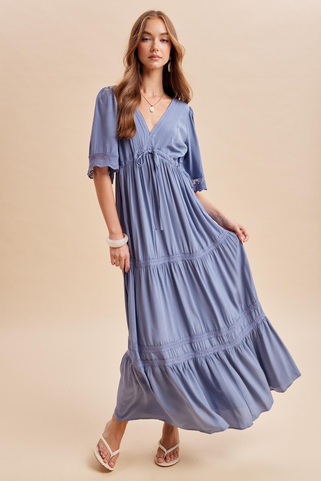 woman wearing a light blue tiered maxi dress with short sleeves and lace details standing in a relaxed pose