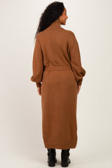 woman wearing a brown long sleeve knitted maternity dress with a high neck and belt detailing, showing her baby bump