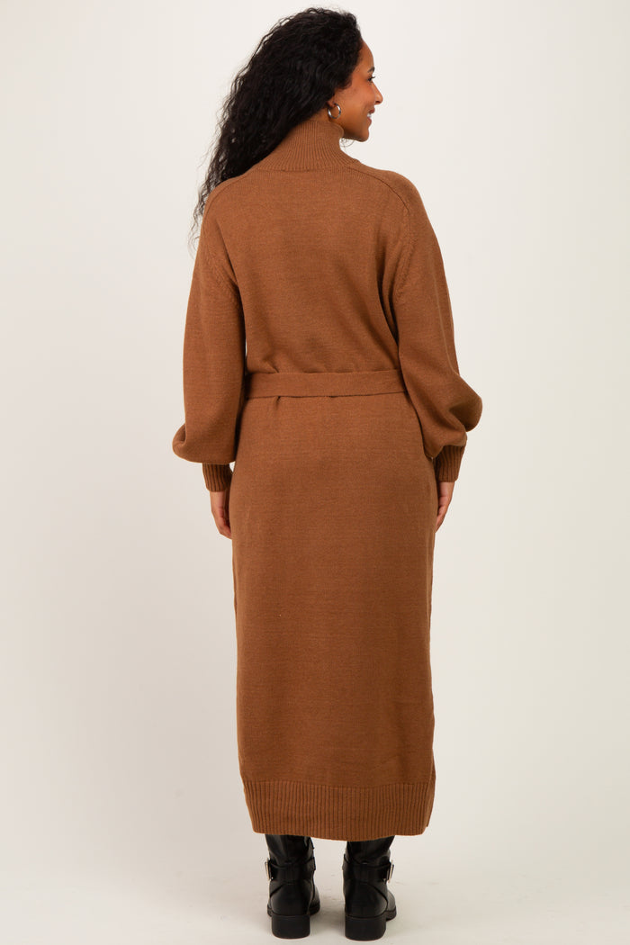 woman wearing a brown long sleeve knitted maternity dress with a high neck and belt detailing, showing her baby bump