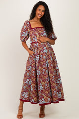 woman wearing a maroon and blue floral print maternity dress with puff sleeves and pockets, showing her baby bump