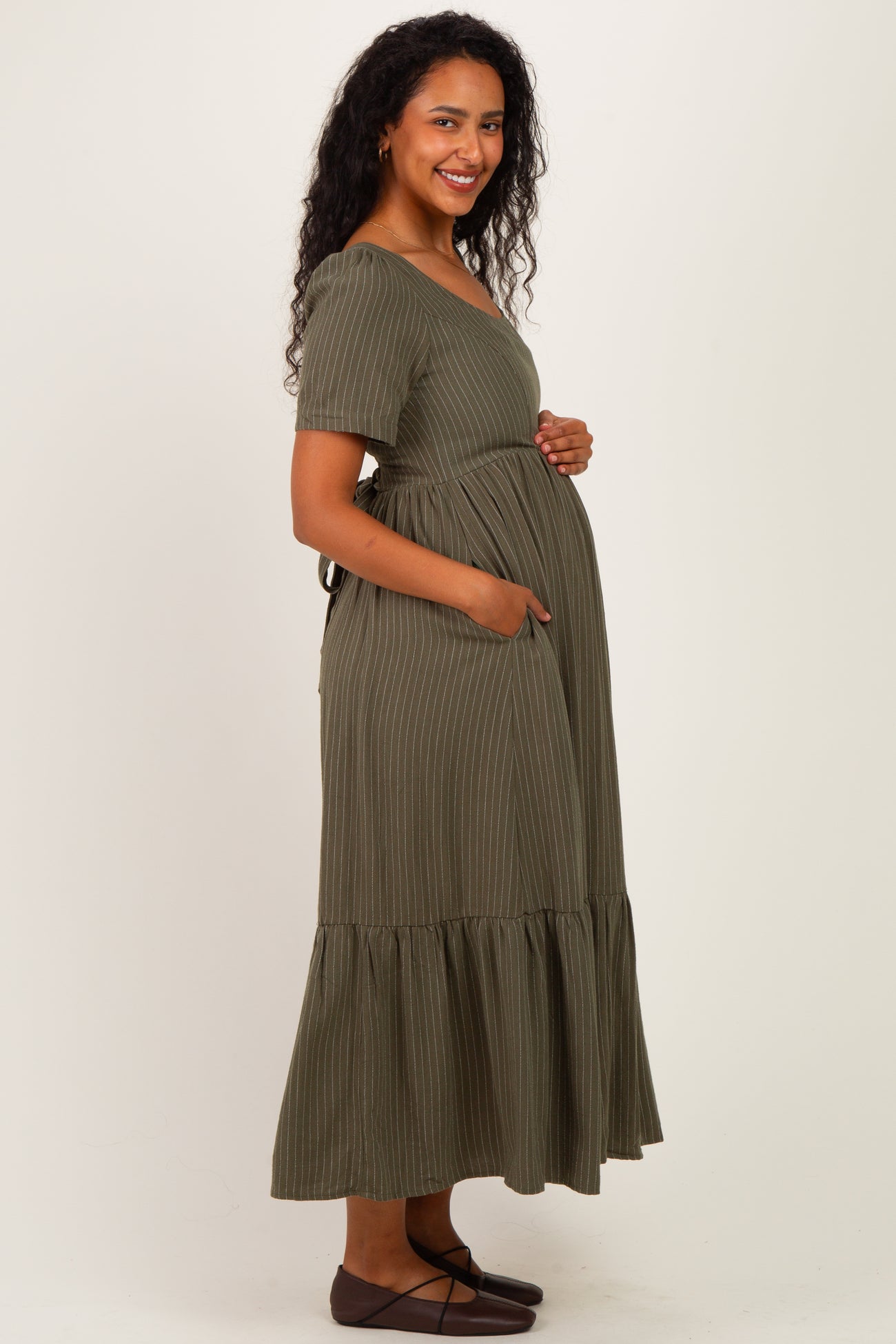woman wearing a green striped maternity maxi dress with short sleeves and pockets, showing her baby bump