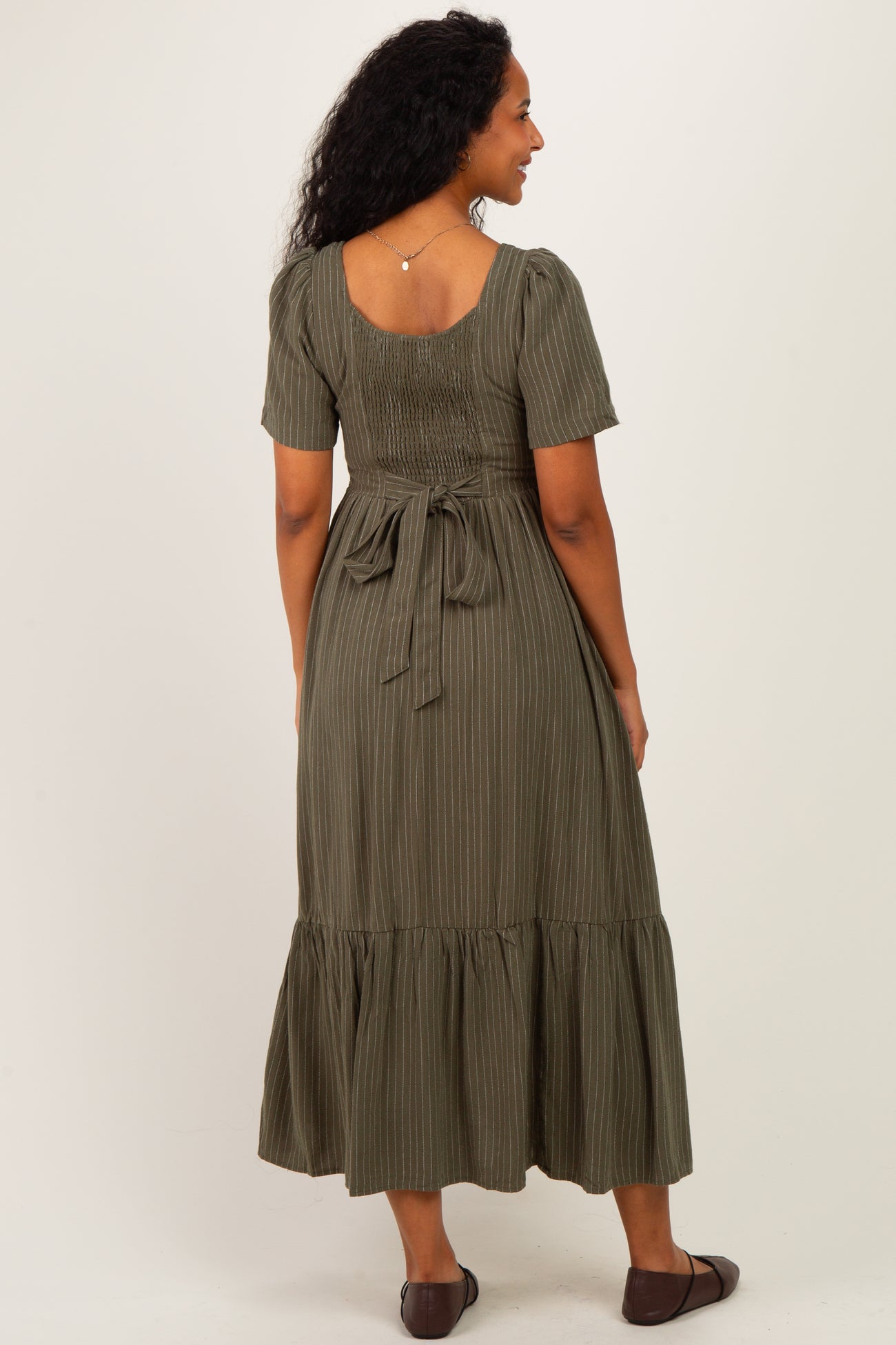 woman wearing a green striped maternity dress with a fitted bodice and a ruffled hem, showing her baby bump from the back