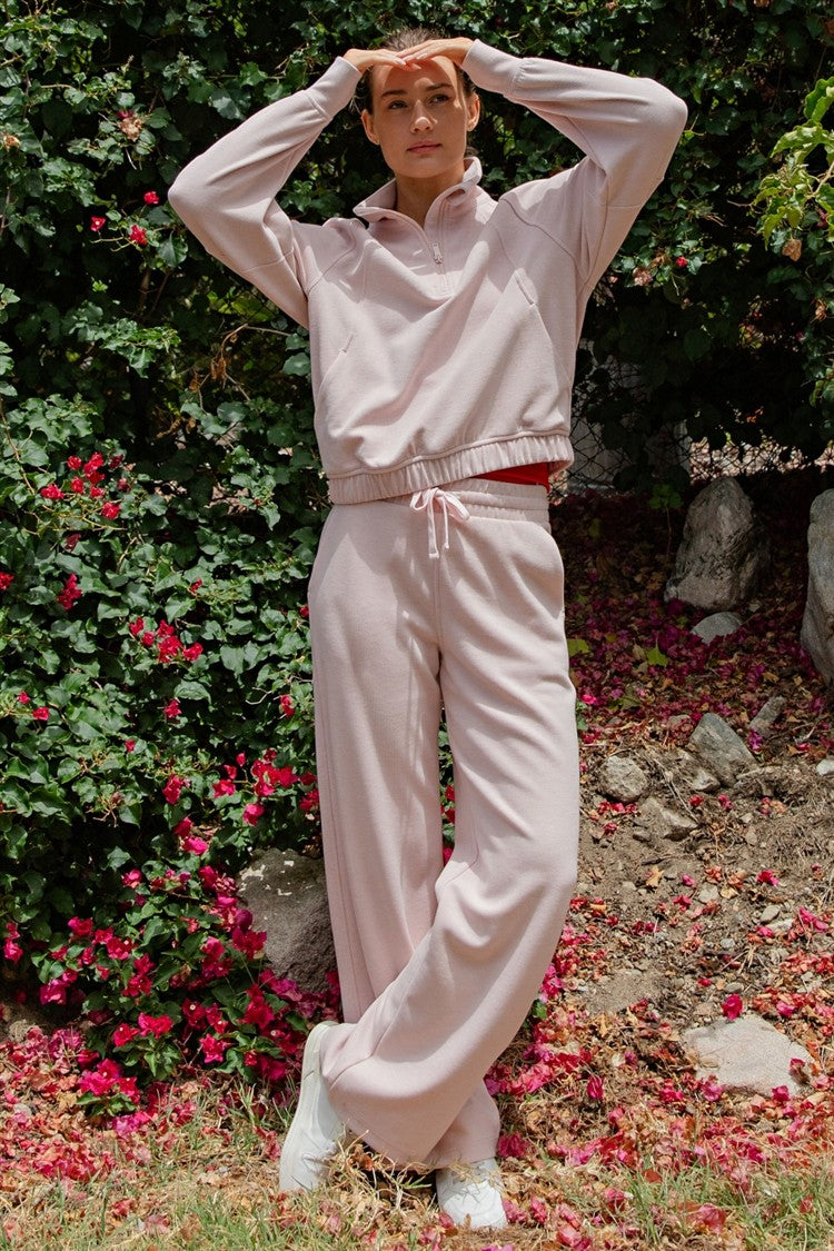 woman wearing a light pink long sleeve crop sweatshirt and matching wide-leg pants with a drawstring waist