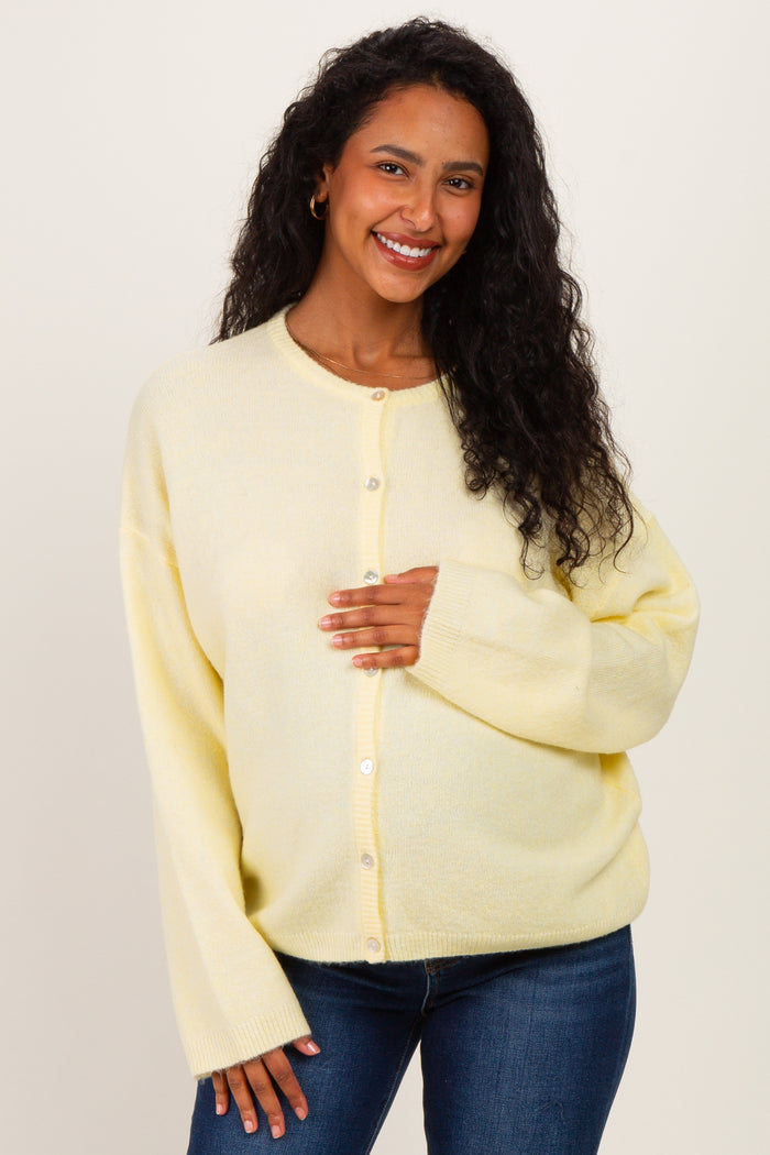 woman wearing a soft yellow maternity cardigan, holding her baby bump, paired with blue jeans