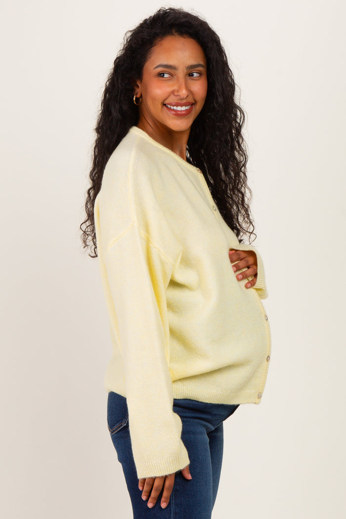 woman wearing a yellow maternity cardigan with buttons and a visible baby bump, paired with dark jeans