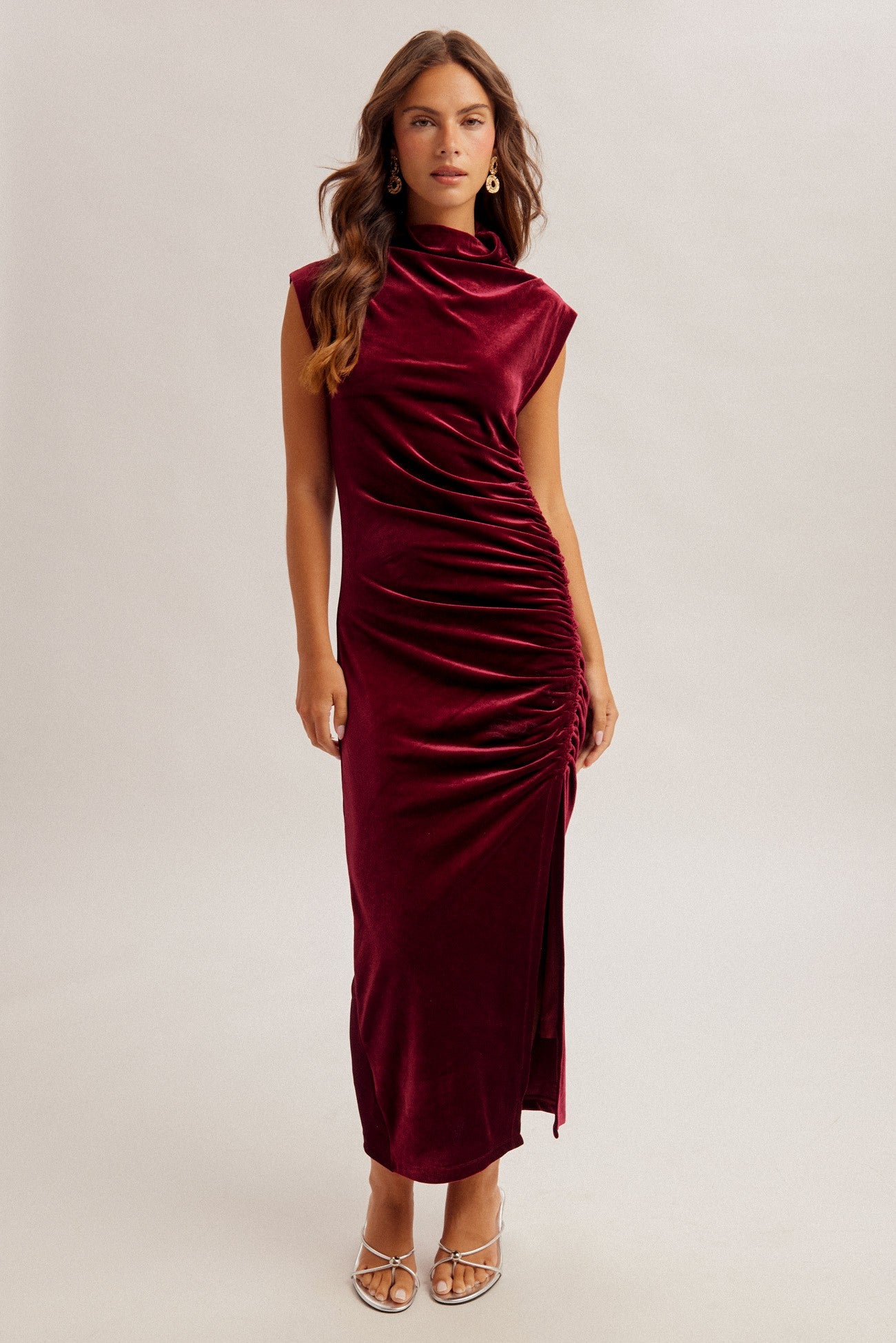 woman wearing a burgundy velvet sleeveless midi dress with side ruching and a high neckline
