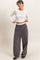 woman wearing a white long sleeve crop top and loose gray wide-leg pants, posing with hands on hips