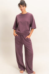 woman wearing a loose-fitting mauve t-shirt and matching wide-leg pants, standing with hands in pockets