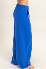 woman wearing bright blue wide-leg pants with pockets, side view, standing barefoot