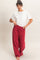 woman wearing a white short sleeve t-shirt and red wide-leg pants, standing with hands in pockets