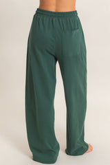 woman wearing green wide-leg lounge pants with an elastic waistband and a back pocket, viewed from the back