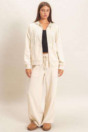 woman wearing a cream colored ribbed hoodie and matching wide leg pants, standing in a relaxed pose