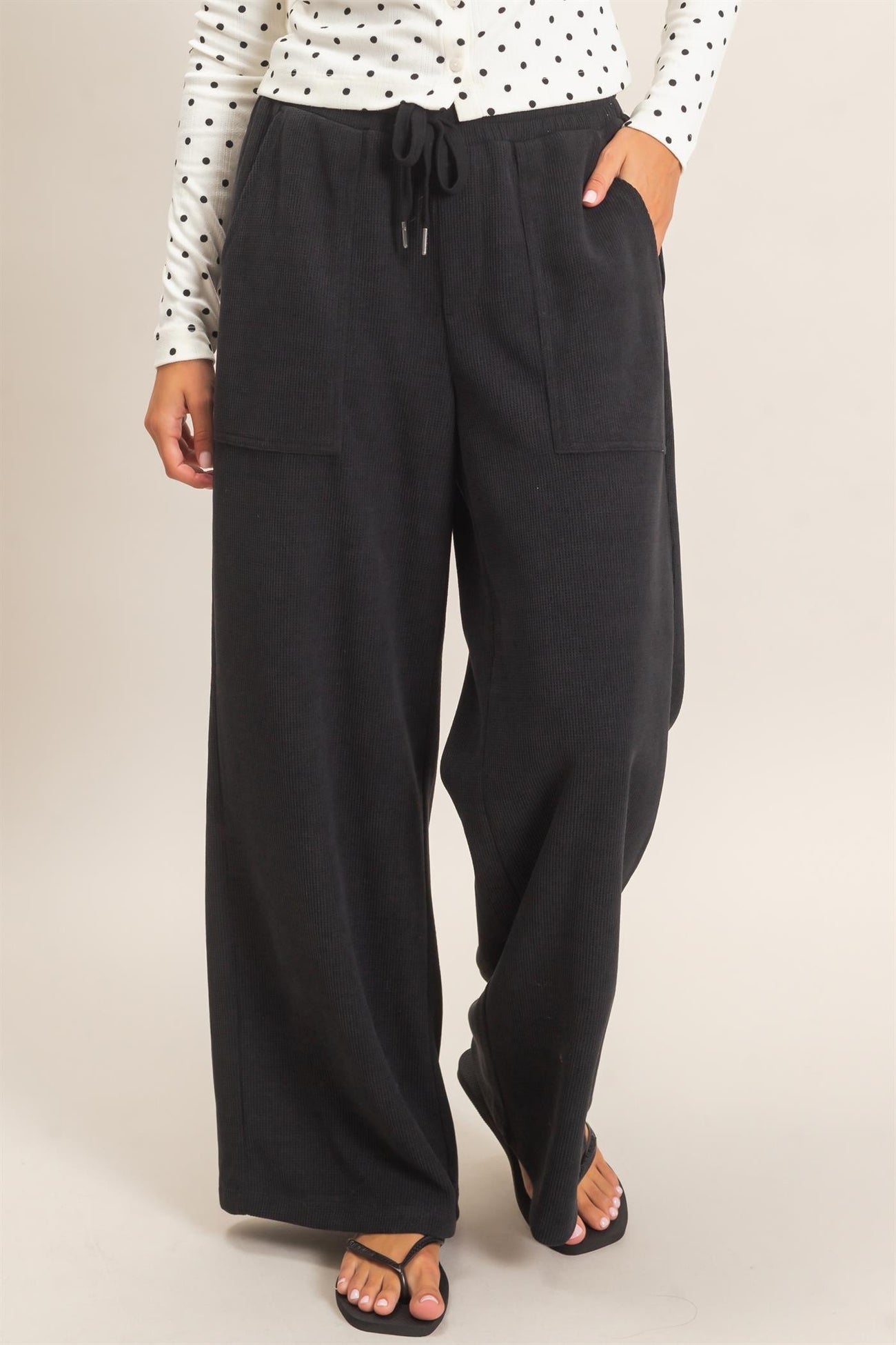 woman wearing black wide-leg lounge pants with side pockets and drawstring waist, styled with a polka dot long sleeve top