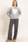 woman wearing a grey sweater with a white heart graphic and grey wide-leg pants, standing with hands on hips
