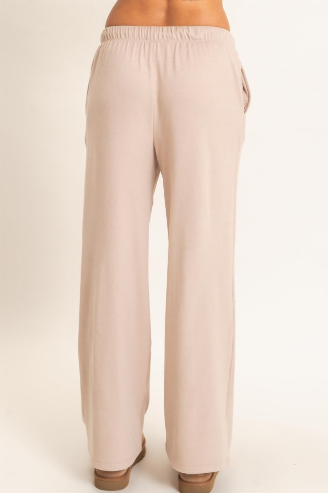 woman wearing light beige wide-leg pants with an elastic waistband and side pockets, viewed from the back