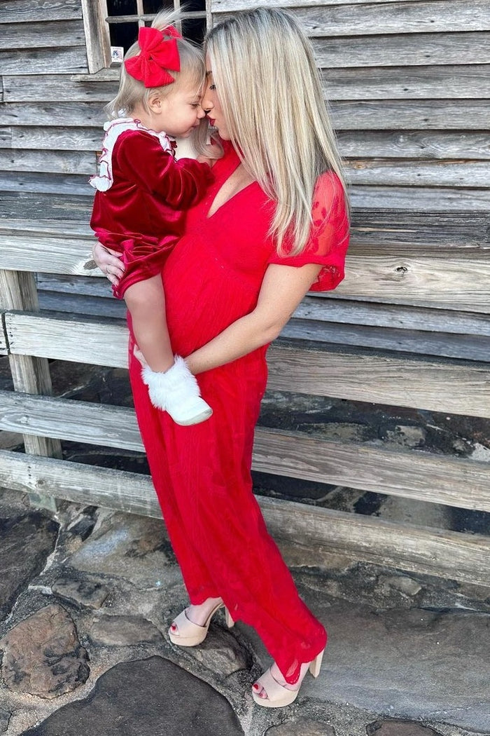 woman wearing a red maternity dress and holding her daughter in front of a wooden background