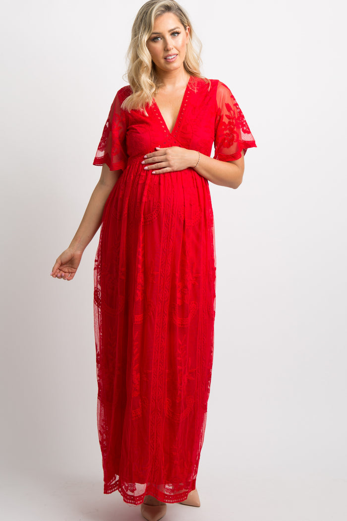 woman wearing a red lace maternity dress, gently cradling her baby bump with a Christmas tree in the background