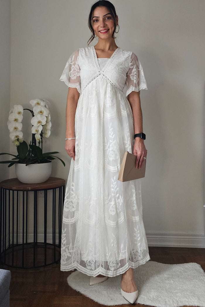 woman wearing a white lace maxi dress with short sleeves and a v-neckline, holding a clutch purse