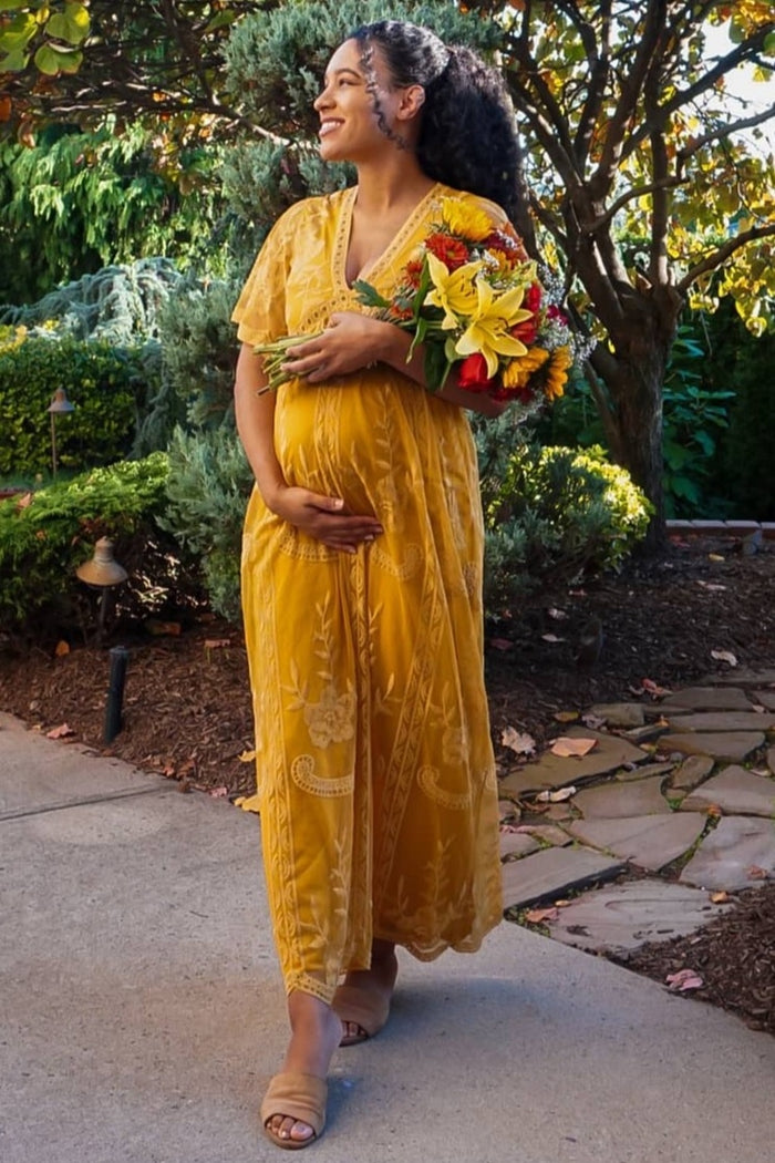 woman wearing a yellow maternity dress with floral details and holding a bouquet, showing her baby bump