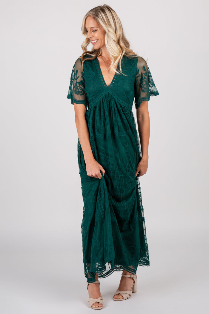 woman wearing a dark green lace maxi dress with short flutter sleeves and beige heels