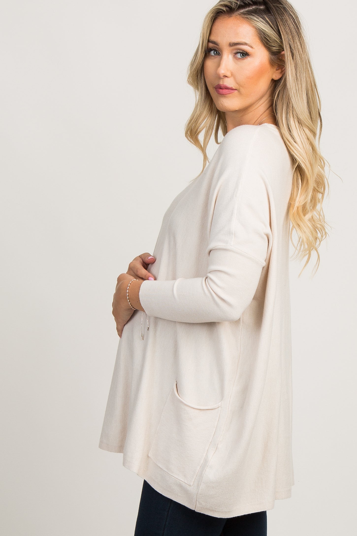 pregnant woman in a cream long sleeve maternity tunic top with pockets standing against a white background