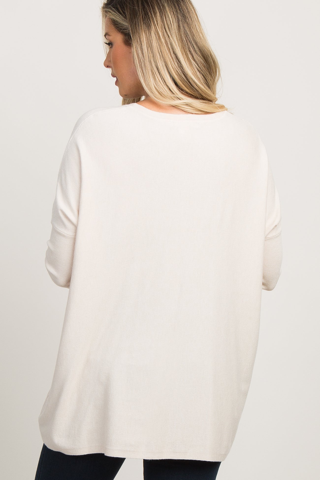 Back view of a woman wearing an oversized cream knit sweater with drop shoulders and ribbed cuffs