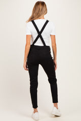 woman wearing black maternity overalls with a white short sleeve top, showing the back view and adjustable straps
