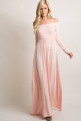 woman wearing a light pink off-the-shoulder maxi dress with long sleeves and a fitted bodice