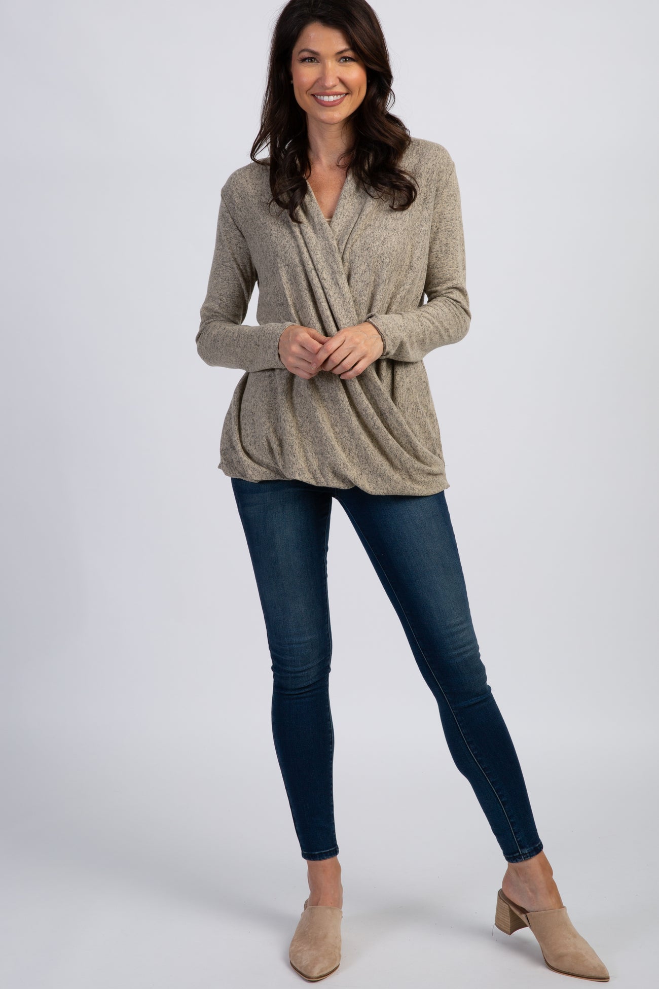 woman wearing a beige wrap-style long sleeve top with draped detailing and blue skinny jeans