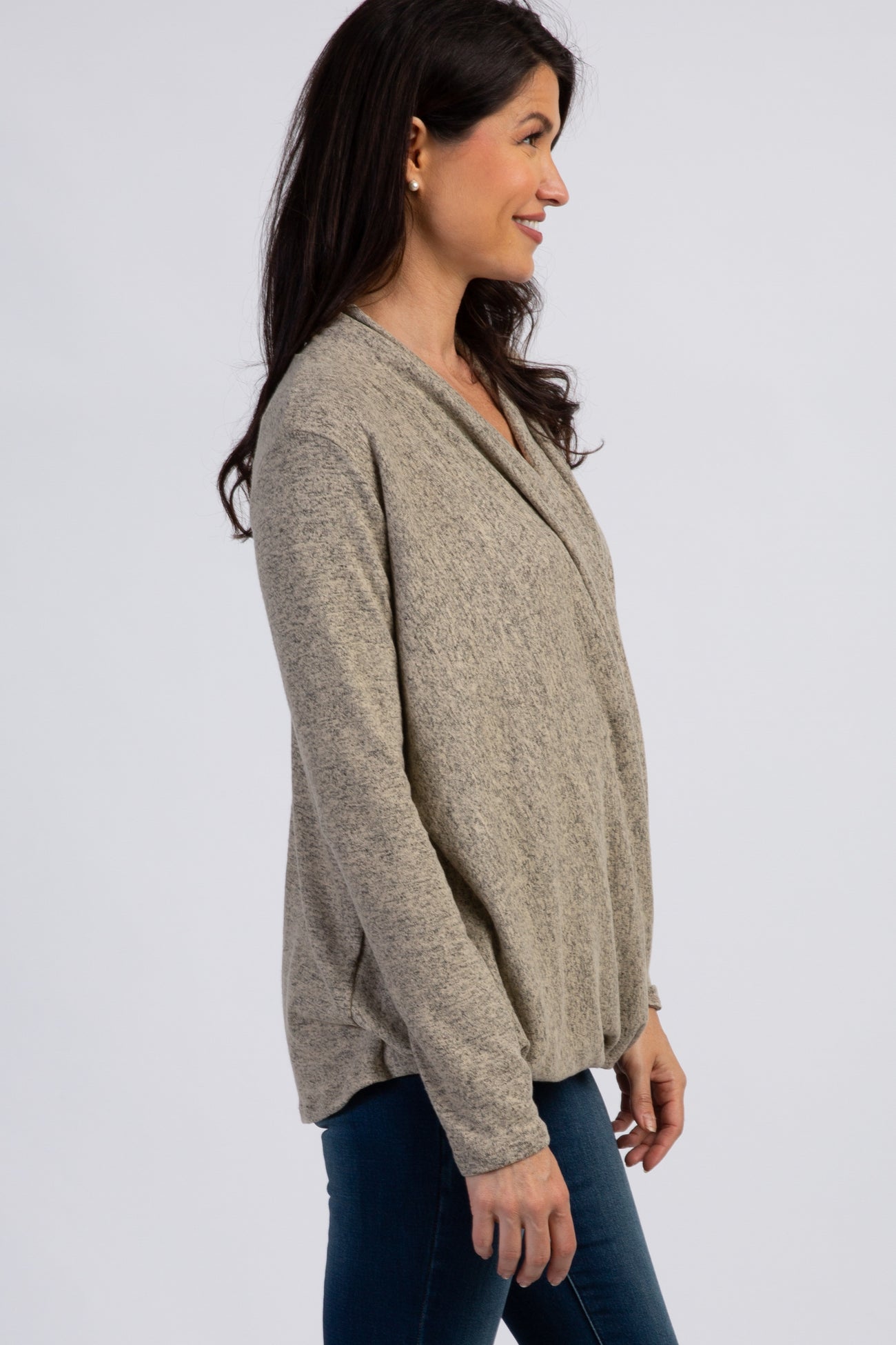 woman wearing a light gray slouchy sweater with a crossover front and long sleeves, paired with dark jeans